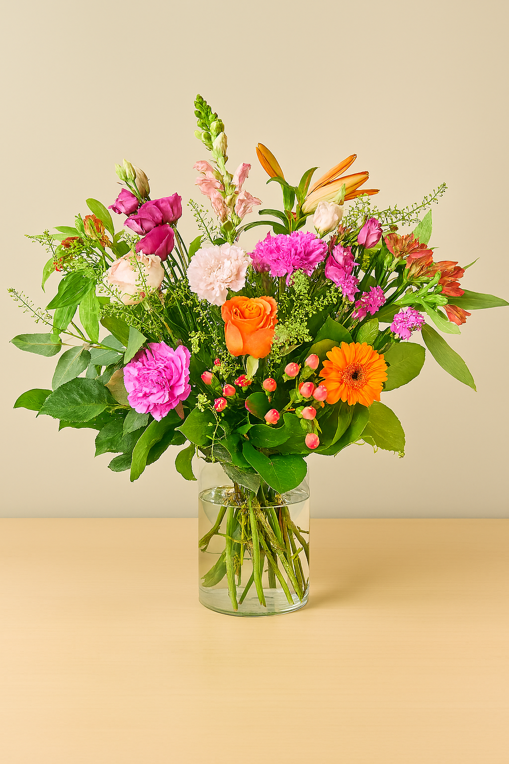 Bunter Blumenstrauß mit orangefarbener Gerbera, orangefarbener Rose, pinken und lila Blüten, Lilien und grünem Beiwerk in Glasvase auf Holztisch.