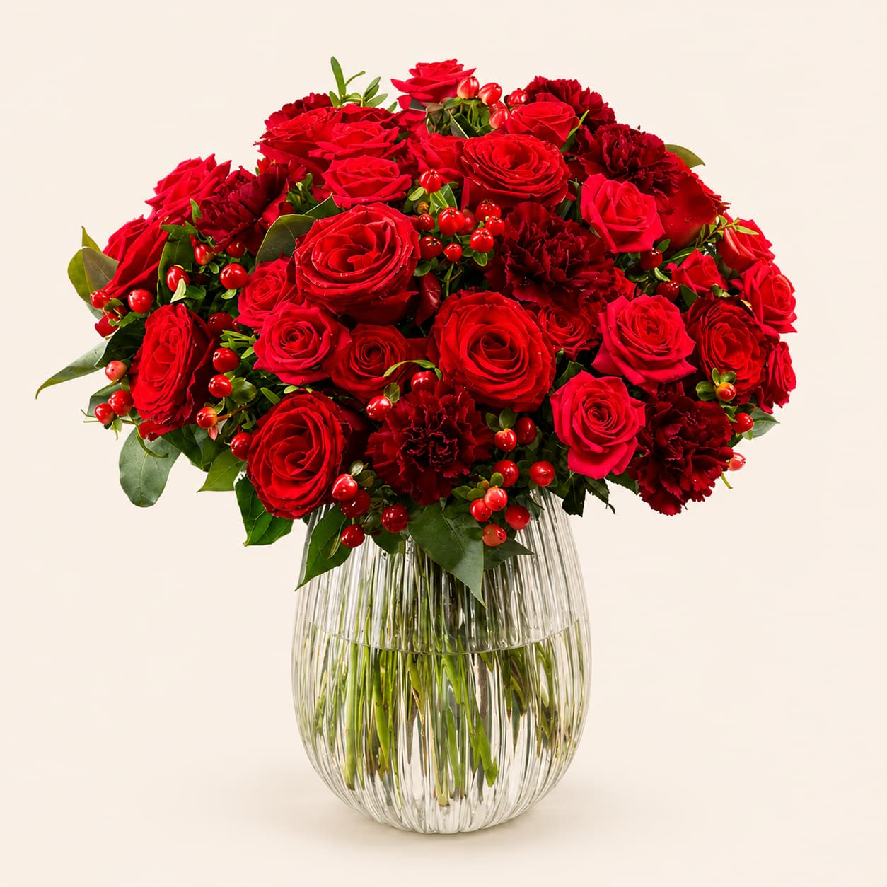 Üppiger roter Blumenstrauß mit roten Rosen, Nelken und Johanniskraut-Beeren in einer geriffelten Glasvase.