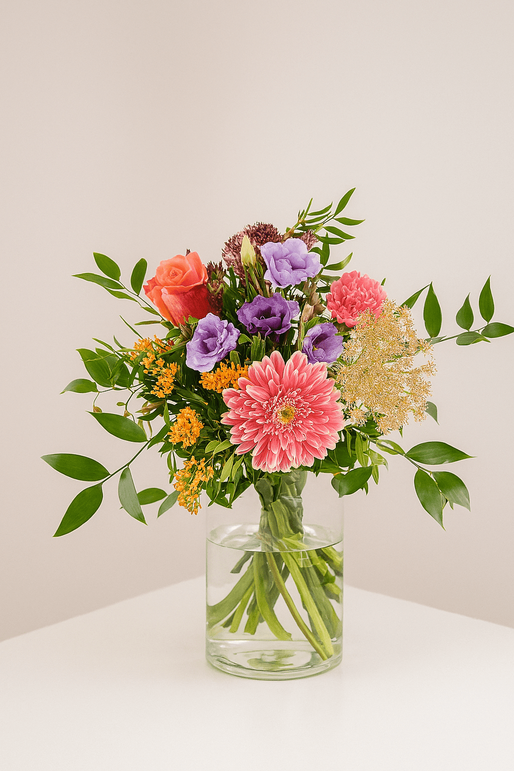 Bunter Blumenstrauß mit pinker Gerbera, orangefarbener Rose, lila Blüten und grünem Beiwerk in Glasvase.